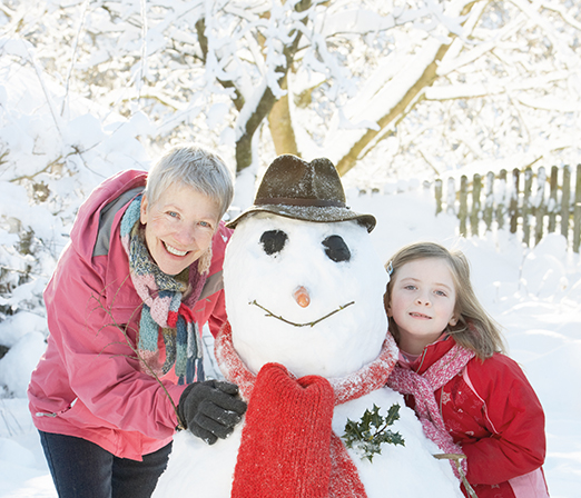 Young Girl With Grandmother Building Snowman In Garden