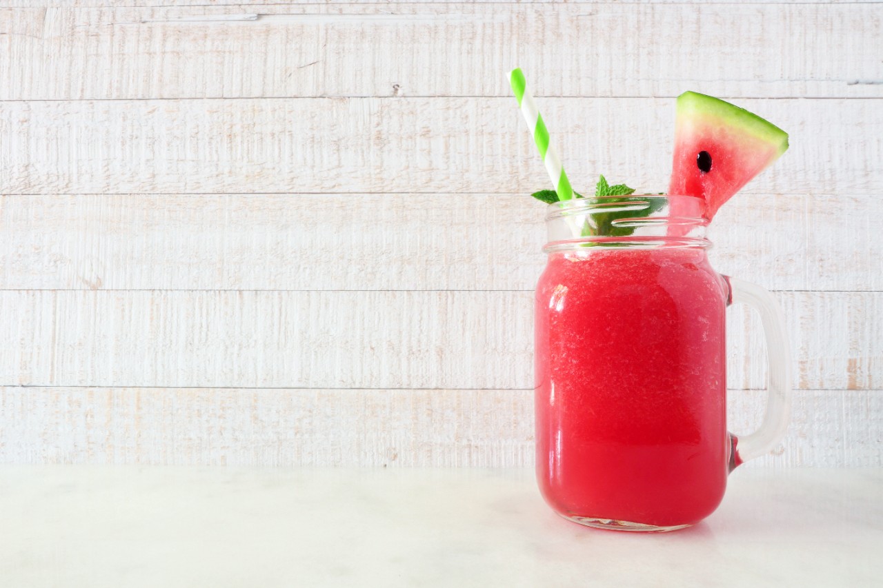 Watermelon juice in a mason jar glass. Side view against a white wood background.